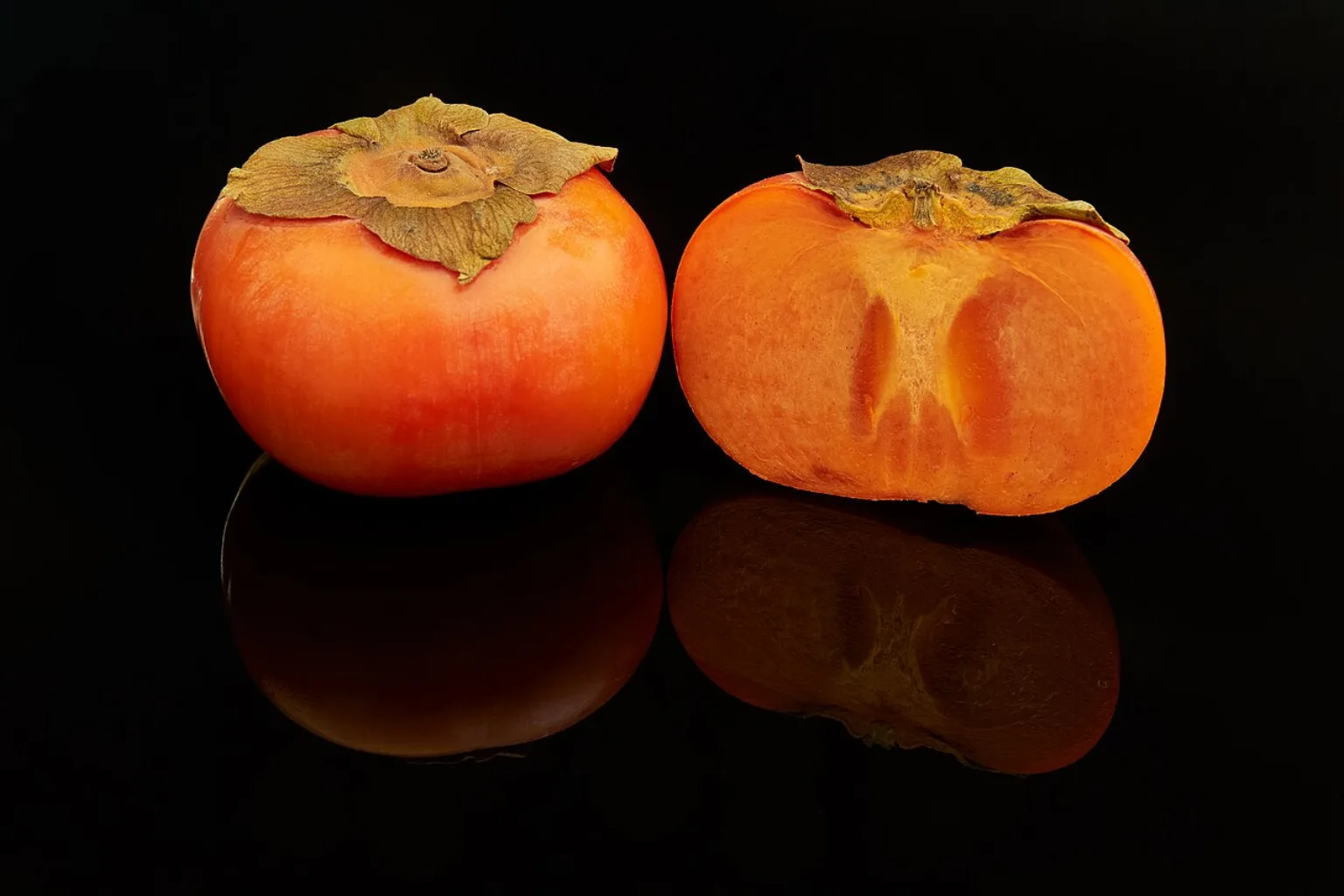 Ripe persimmon fruits, one whole and one cut open to show the flesh