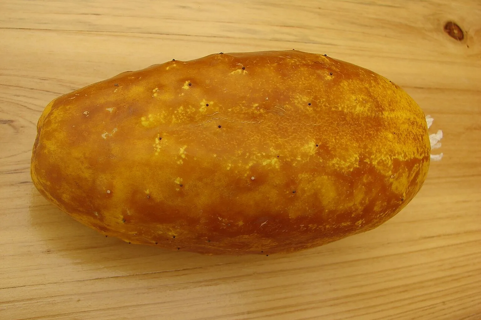 A whole yellow cucumber resting on a wooden worktop